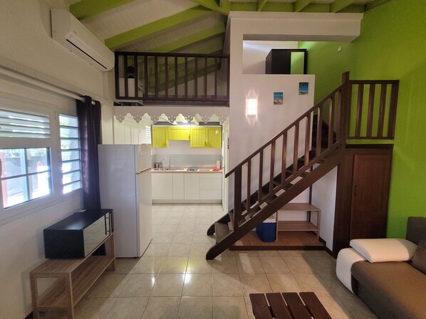 A compact living space with a kitchen, a staircase, a sofa, and a TV.