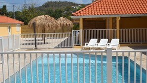 A swimming pool with white lounge chairs and a thatched-roof structure in the background. - Eden Kay - 100m from the beach (Les Trois-Îlets)