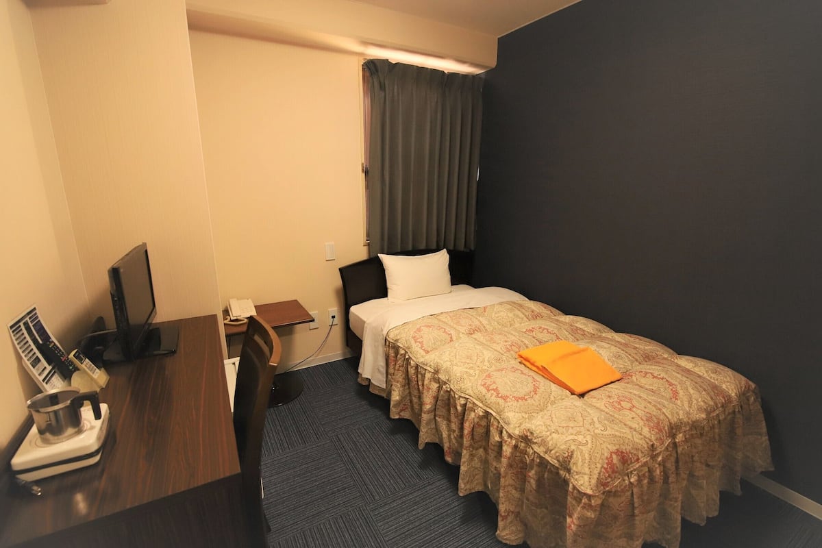 Een hotelkamer met een bed, een bureau met een computer, een telefoon en een raam met gordijnen.