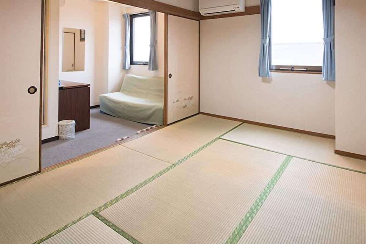 Een traditionele Japanse kamer met tatami vloeren, een schuifdeur, een klein bed, een raam met gordijnen en een airconditioning.