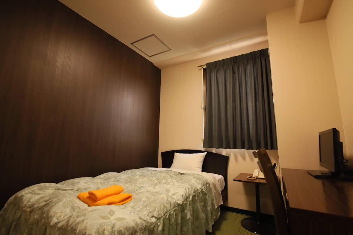Een hotelkamer met een bed, een bureau met een computer, een televisie en een raam met gordijnen.