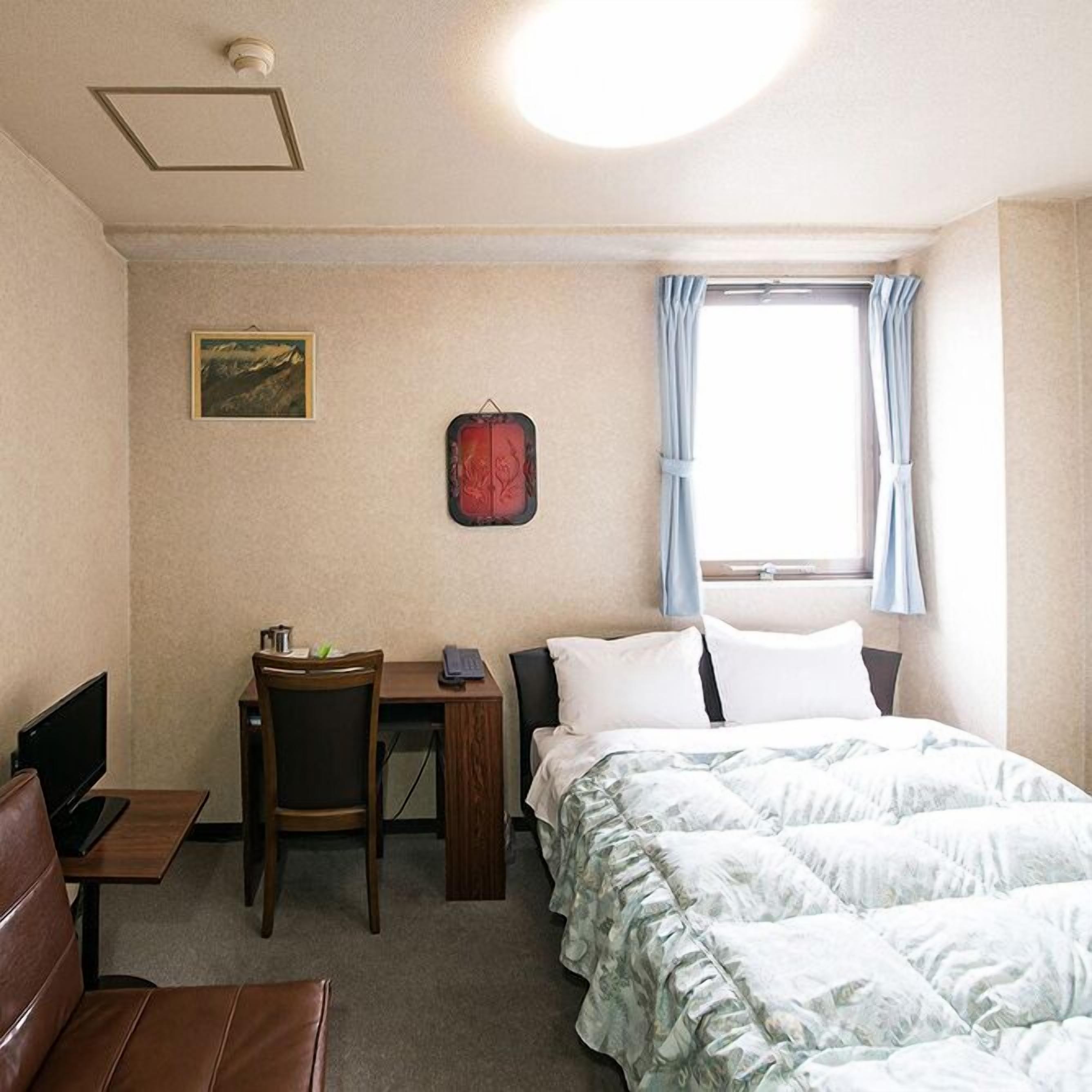 Une chambre d’hôtel équipée d’un lit, d’un bureau, d’une chaise, d’une télévision et d’une fenêtre avec des rideaux.