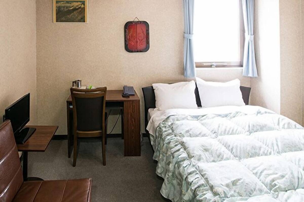 Hotelkamer met een bed, een bureau, een stoel, een televisie en een raam met gordijnen.