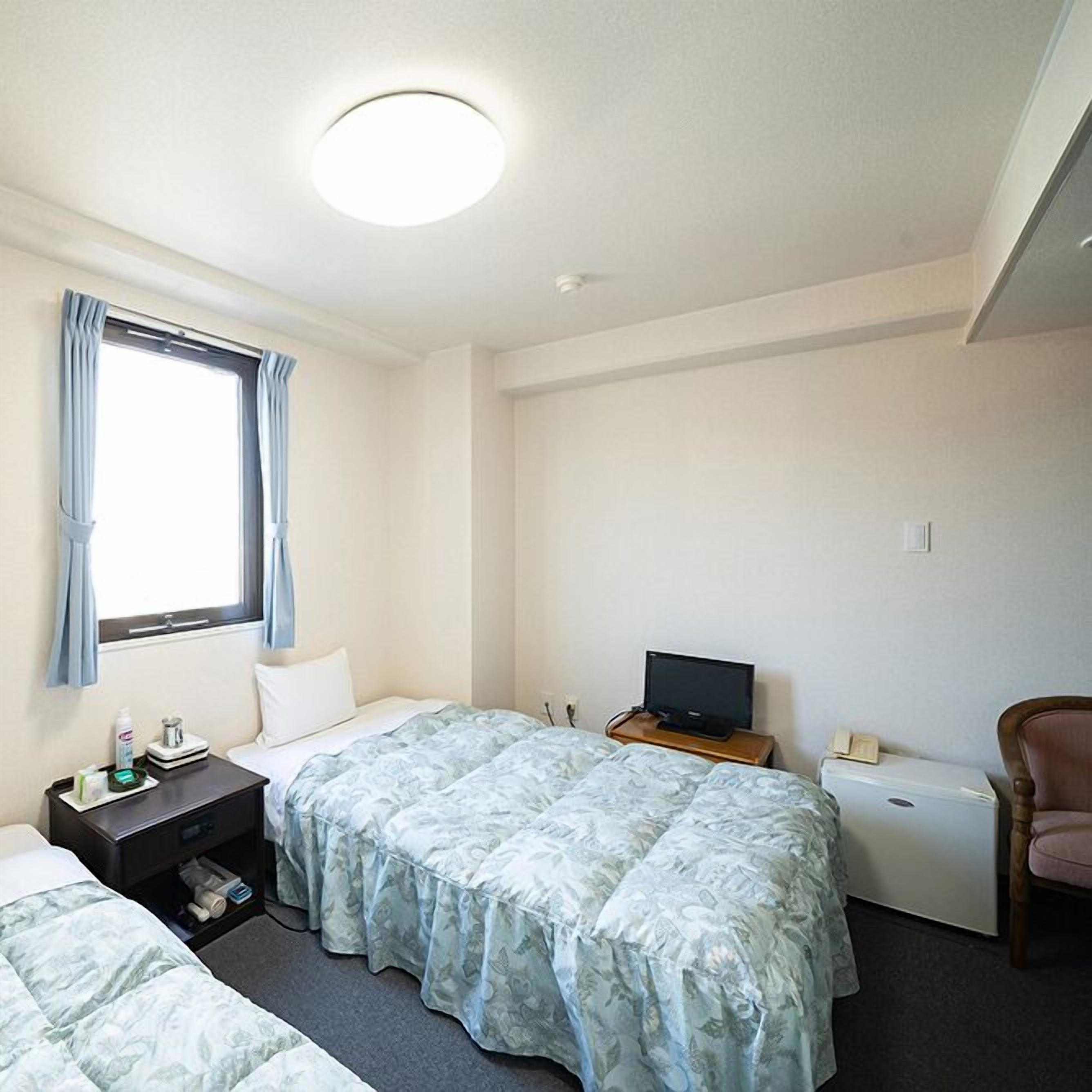 Une chambre d’hôtel avec deux lits, une télévision, une chaise et une petite table avec des articles de toilette.