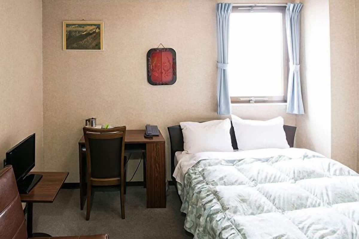 Een hotelkamer met een bed, een bureau met stoel, een televisie en een raam met gordijnen.