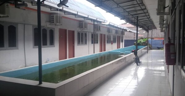 Un espace piscine couvert, situé à côté d’un bâtiment doté de nombreuses fenêtres et portes.