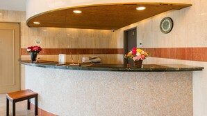 A reception desk with a wooden ceiling, a clock, and two flower arrangements. - Hotel Gen Kikukawa (Kikugawa)