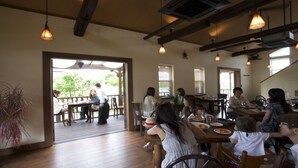 An indoor dining area with wooden tables and chairs, large windows allowing natural light, and hanging pendant lights. - Hotel Gen Kikukawa (Kikugawa)