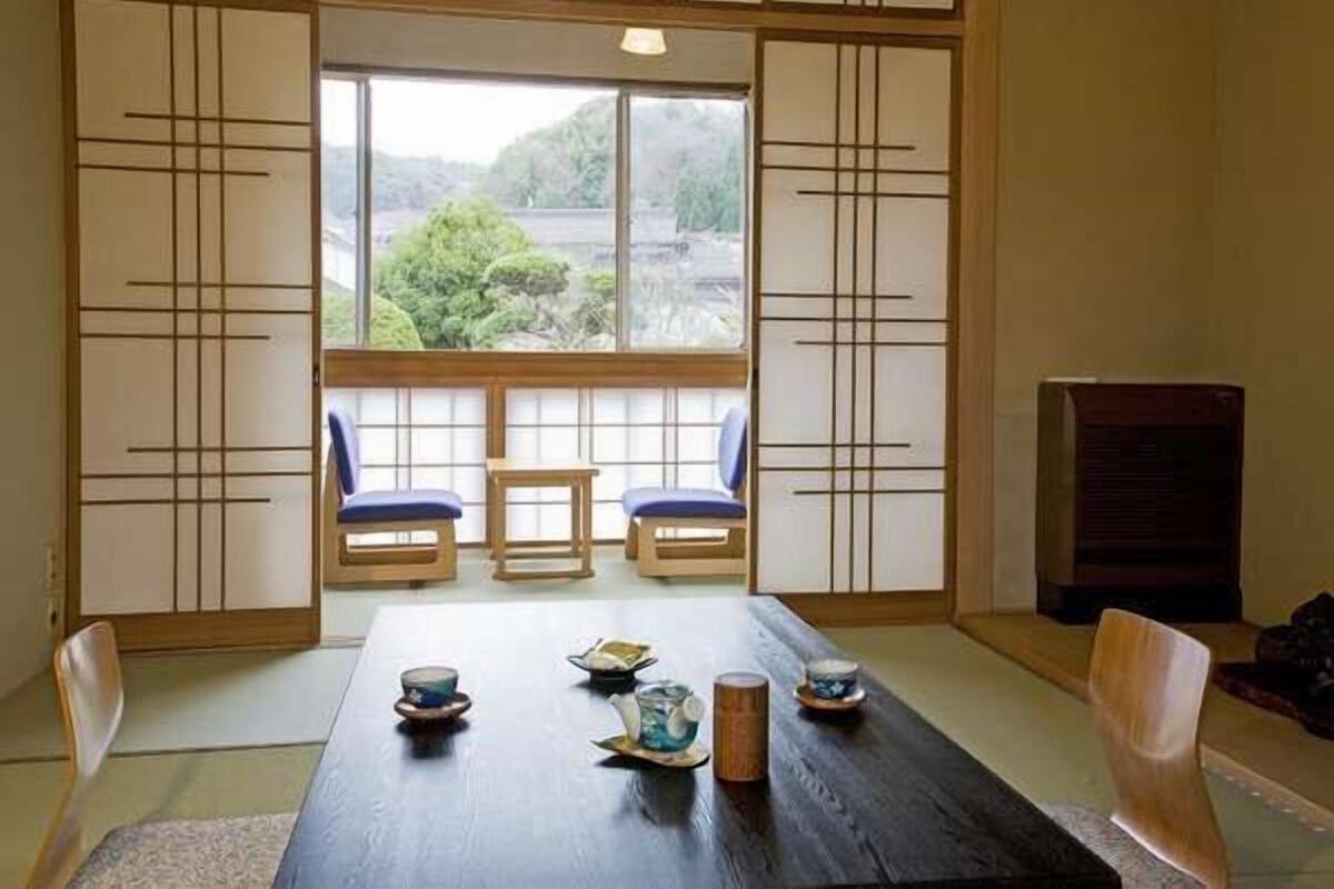 Une pièce de style japonais traditionnel, avec un sol recouvert de tatamis, une petite table basse sur laquelle sont disposés des ensembles à thé, et des portes coulissantes ornées de motifs géométriques.