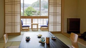 Une pièce de style japonais traditionnel, avec un sol recouvert de tatamis, une petite table basse agrémentée d’un service à thé, et des portes coulissantes donnant sur un paysage verdoyant.