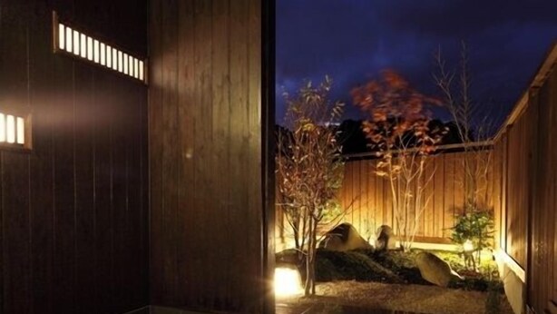 Un bâtiment moderne avec une façade en bois, une entrée carrelée en pierre et un petit jardin agrémenté d’un arbre et d’un banc.