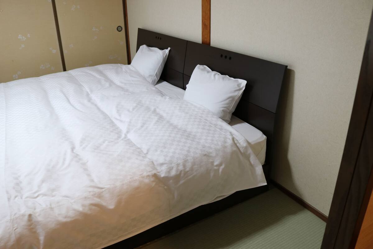 Un lit bien fait, avec une tête de lit sombre, du linge de lit blanc et un papier peint à motifs.