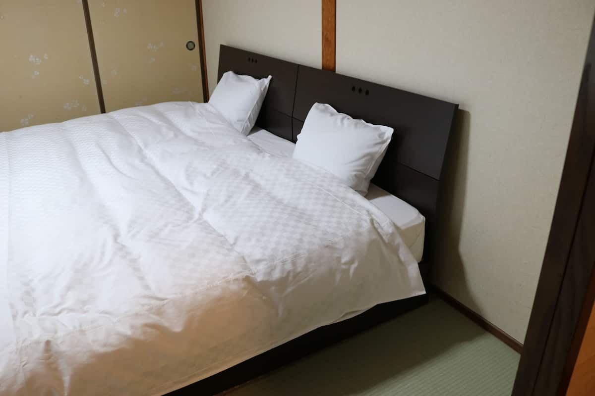 Una cama bien hecha con un cabecero oscuro, ropa de cama blanca y un papel tapiz estampado.