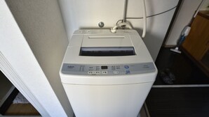 Een voorzichtige kijk op een witte, compacte wasmachine met voorlader en bedieningspaneel, geplaatst in een wasserij met een houten kast en een betegelde vloer.
