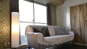Een kamer met een bank, bekleed met een bloemenprint plaid, een staande lamp en een houten kledingkast.