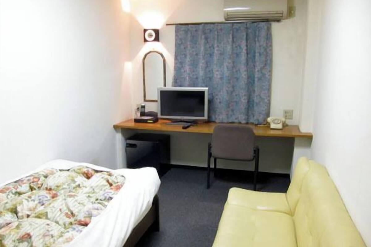 A hotel room with a bed, a desk with a computer, a chair, and a couch.