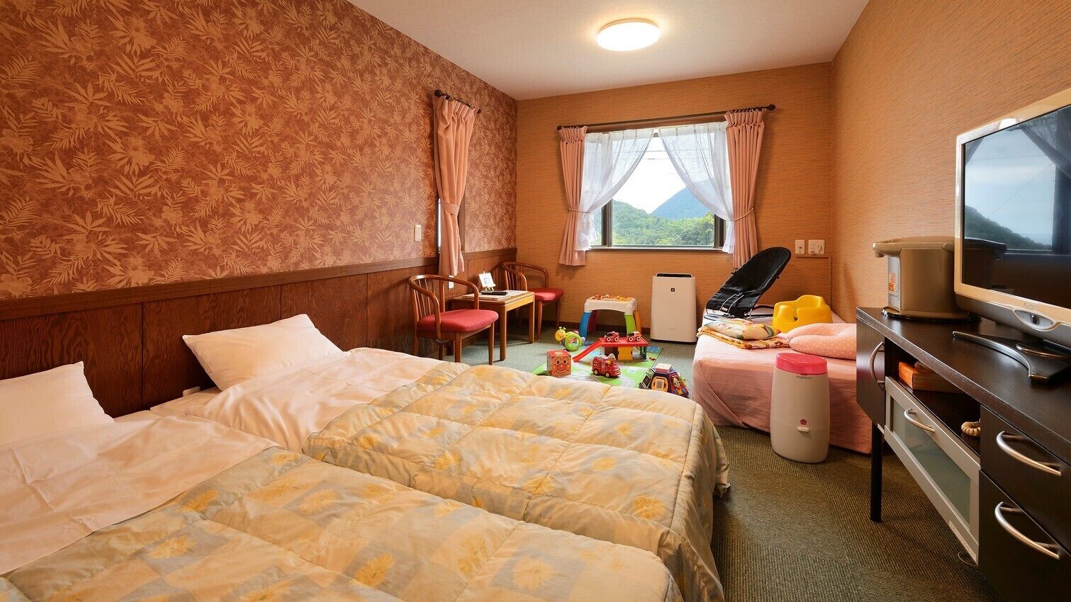 Habitació d'hotel amb dos llits, un escriptori, una cadira, un televisor i una finestra amb vista a la muntanya.
