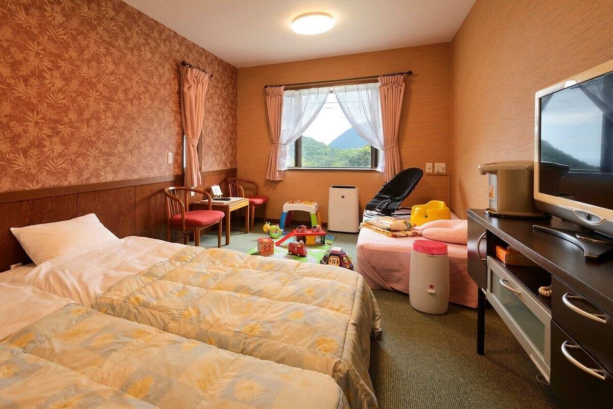 Habitación de hotel con dos camas, un escritorio, una silla, un televisor y una ventana con vista a la montaña.