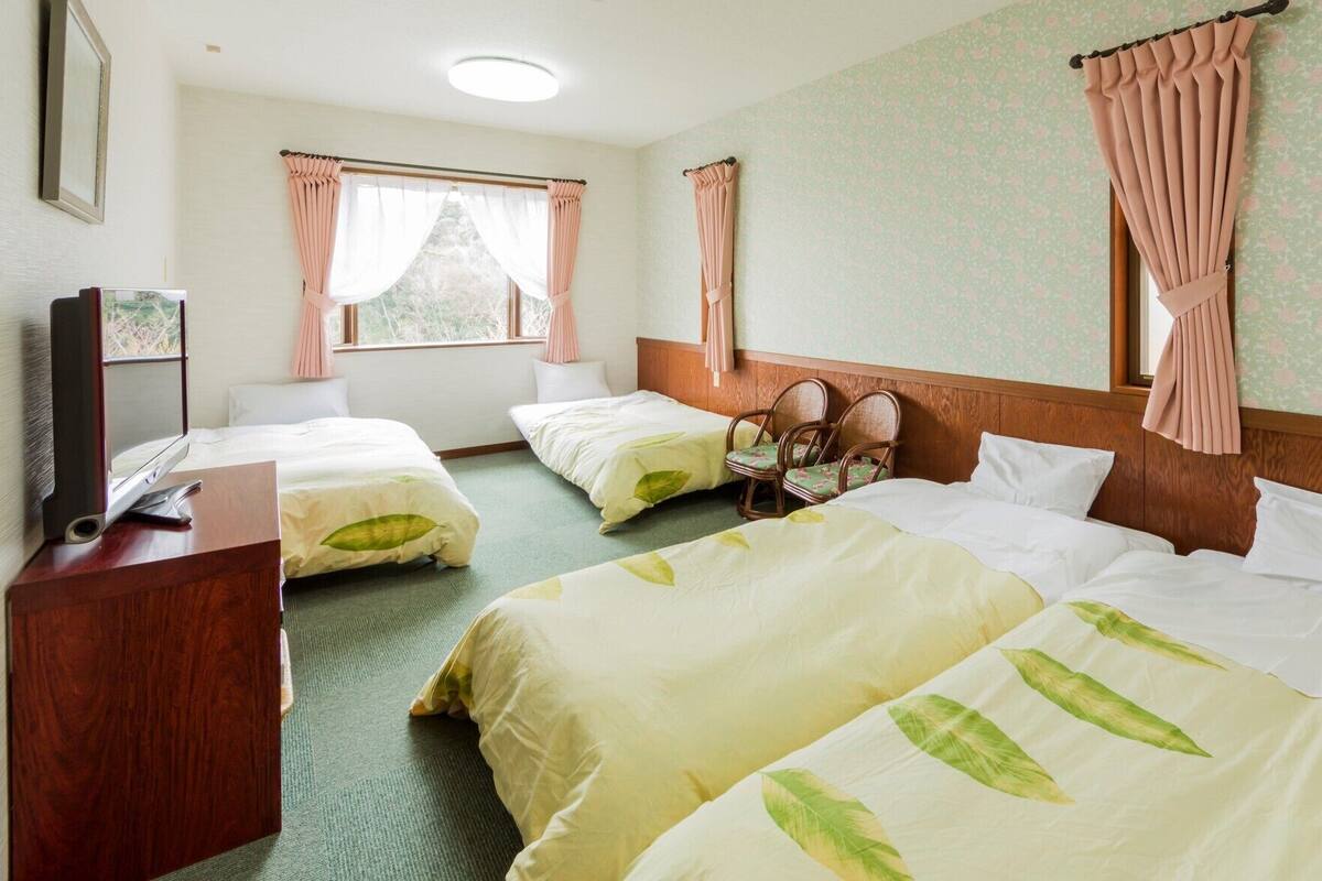 Habitación de hotel con dos camas, cabecero de madera, televisor sobre un mueble de madera y ventana con cortinas.