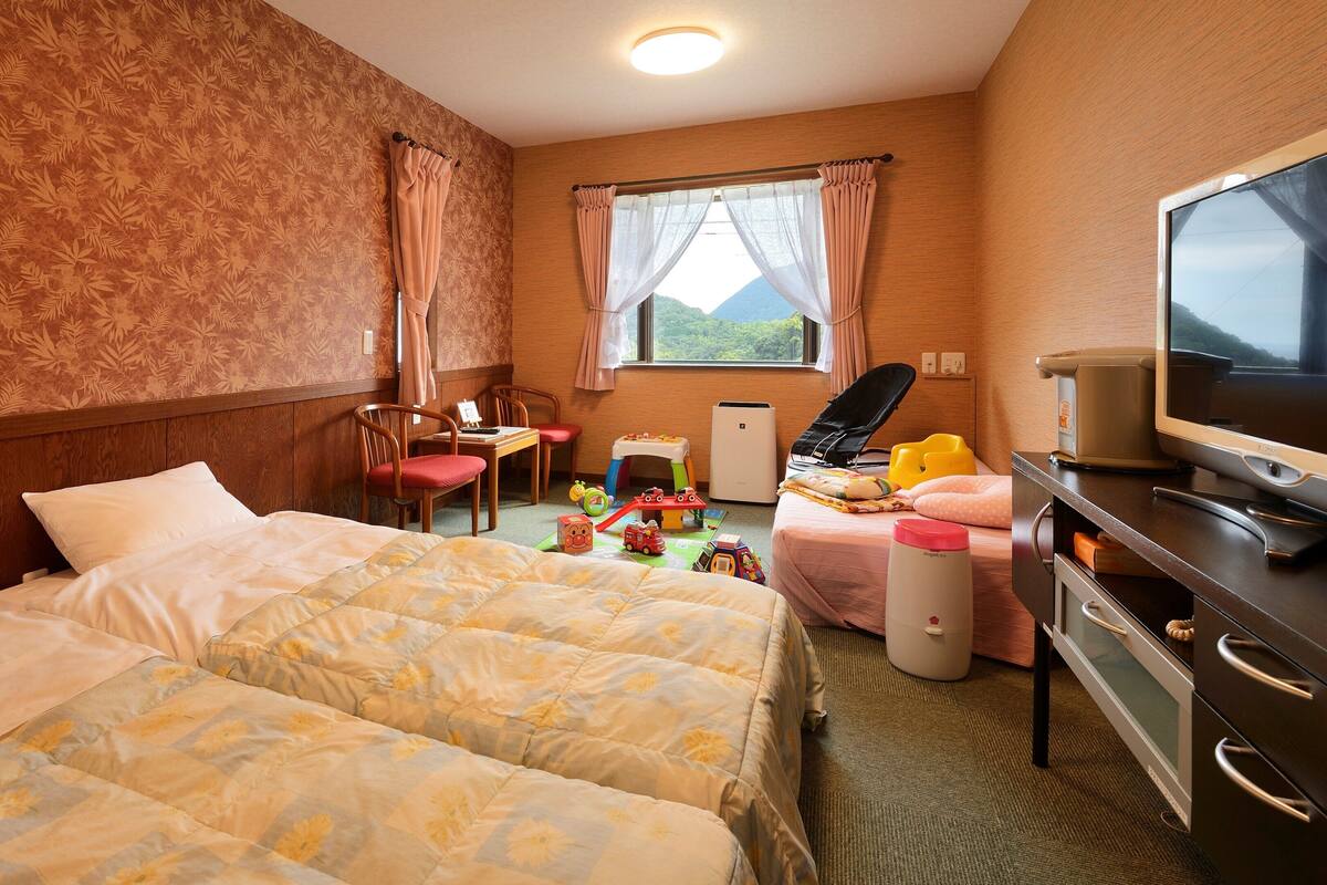 Una habitación de hotel con dos camas, un escritorio, una silla, un televisor y una ventana con cortinas.