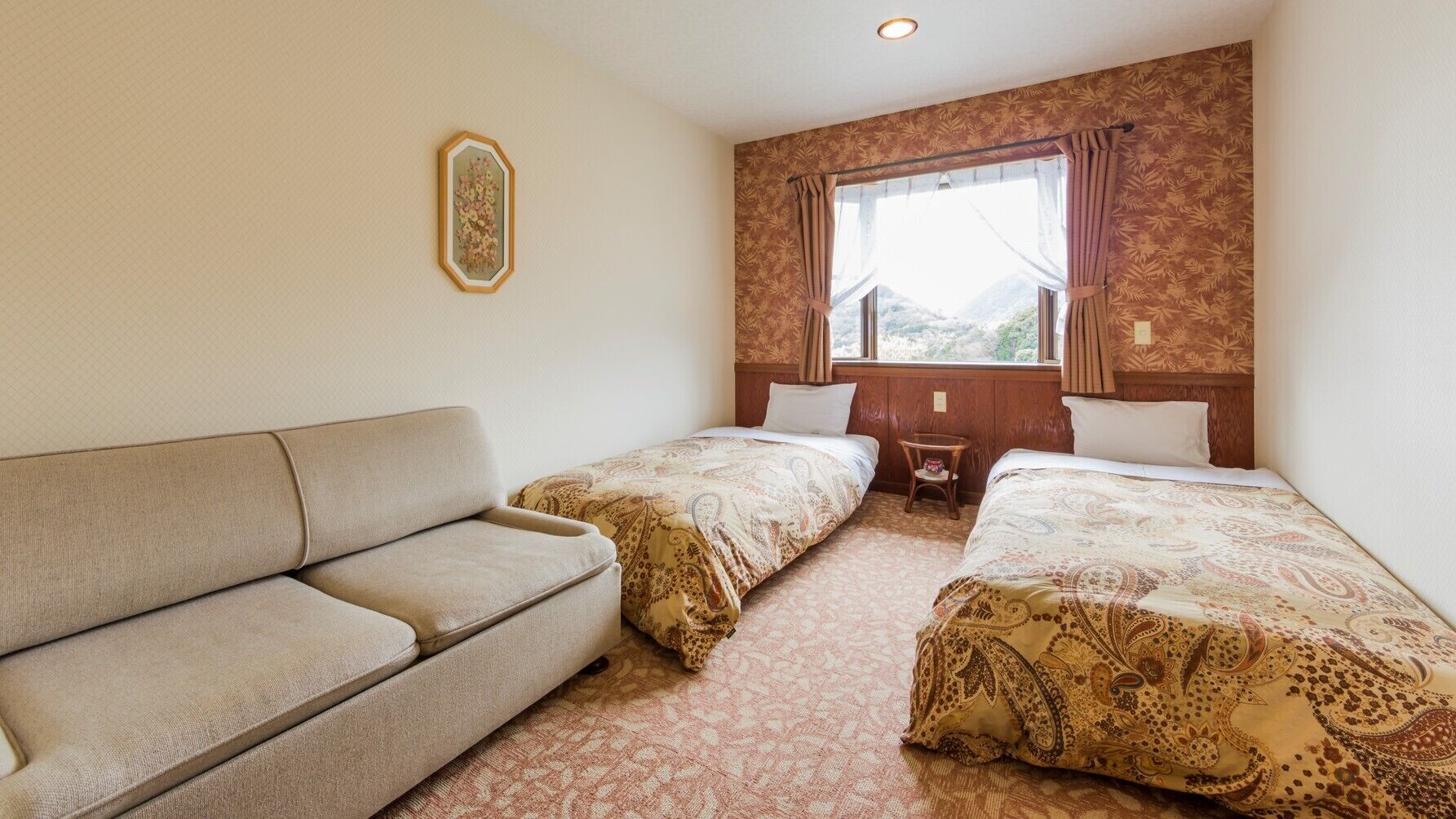 Habitació d'hotel amb sofà, dos llits individuals, una taula petita i una finestra amb cortines.
