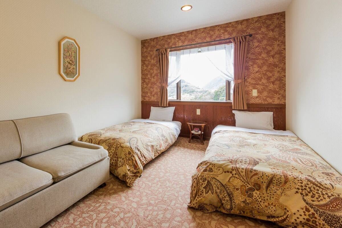 Una habitación de hotel con sofá, dos camas individuales, una mesita y una ventana con cortinas.