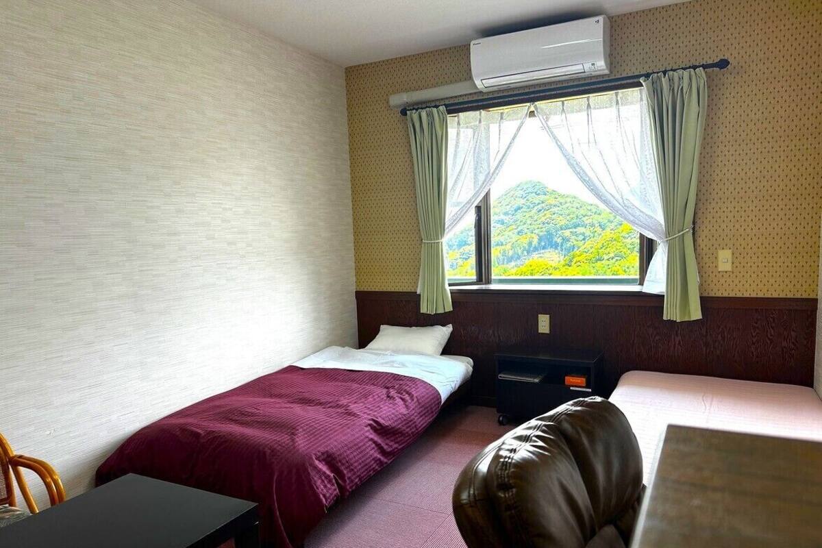 Una habitación con dos camas, un escritorio, una silla, aire acondicionado y una ventana con cortinas.