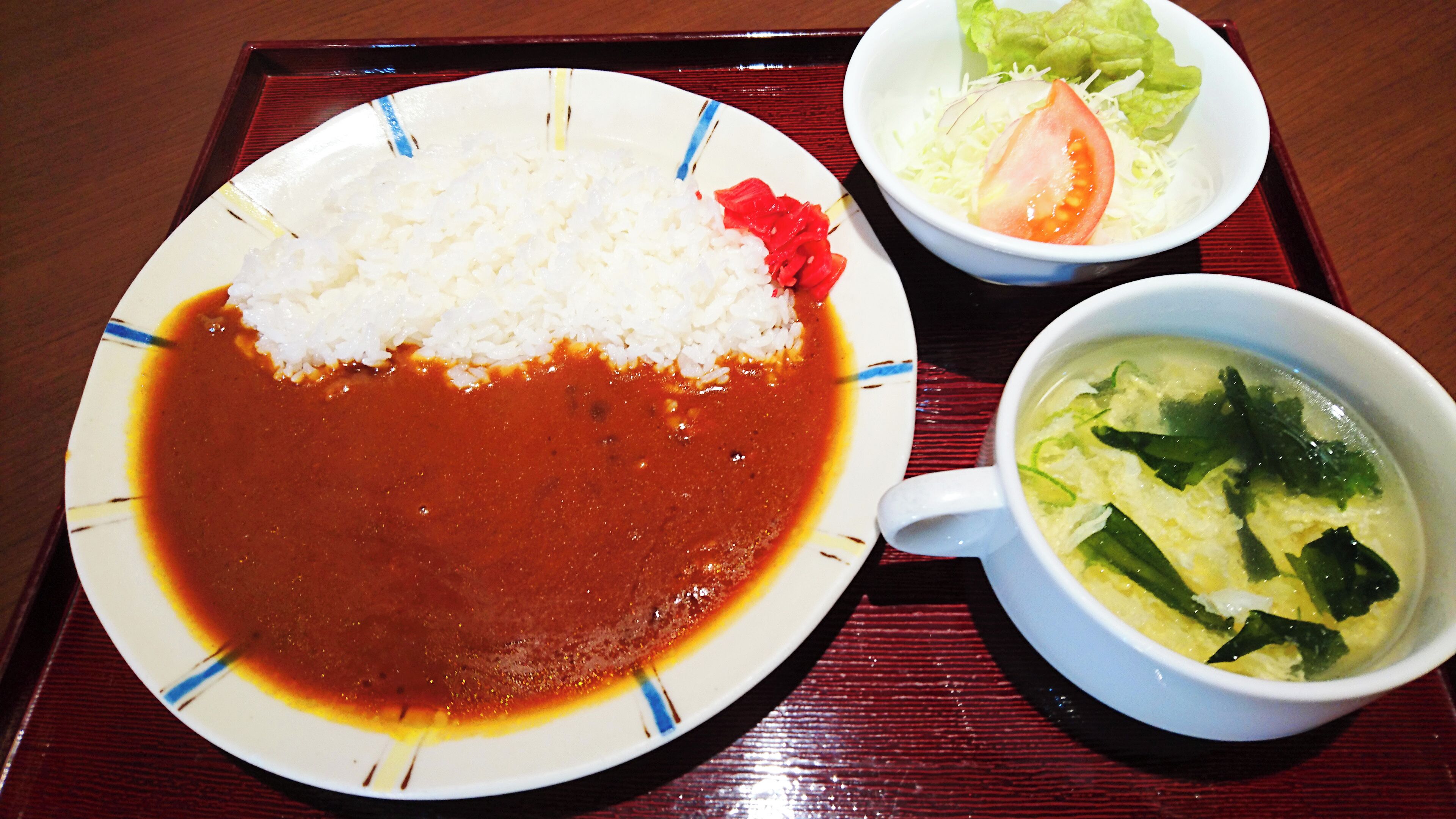 A plate of white rice with red sauce, a bowl of soup with vegetables, and a small bowl of salad with lettuce and tomato on a tray.