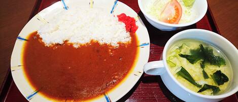 A plate of white rice with red sauce, a bowl of soup with vegetables, and a small bowl of salad with lettuce and tomato on a tray.