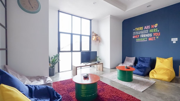 A modern living room with a large window, a flat-screen TV, a sofa, a coffee table, and a wall with motivational text. - Fello Bnb Hostel Kuta - Adults Only (Kuta)