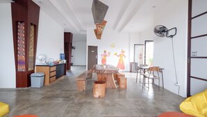 A spacious living area with a wooden coffee table, seating arrangements, and a kitchen area with a water dispenser. - Fello Bnb Hostel Kuta - Adults Only (Kuta)