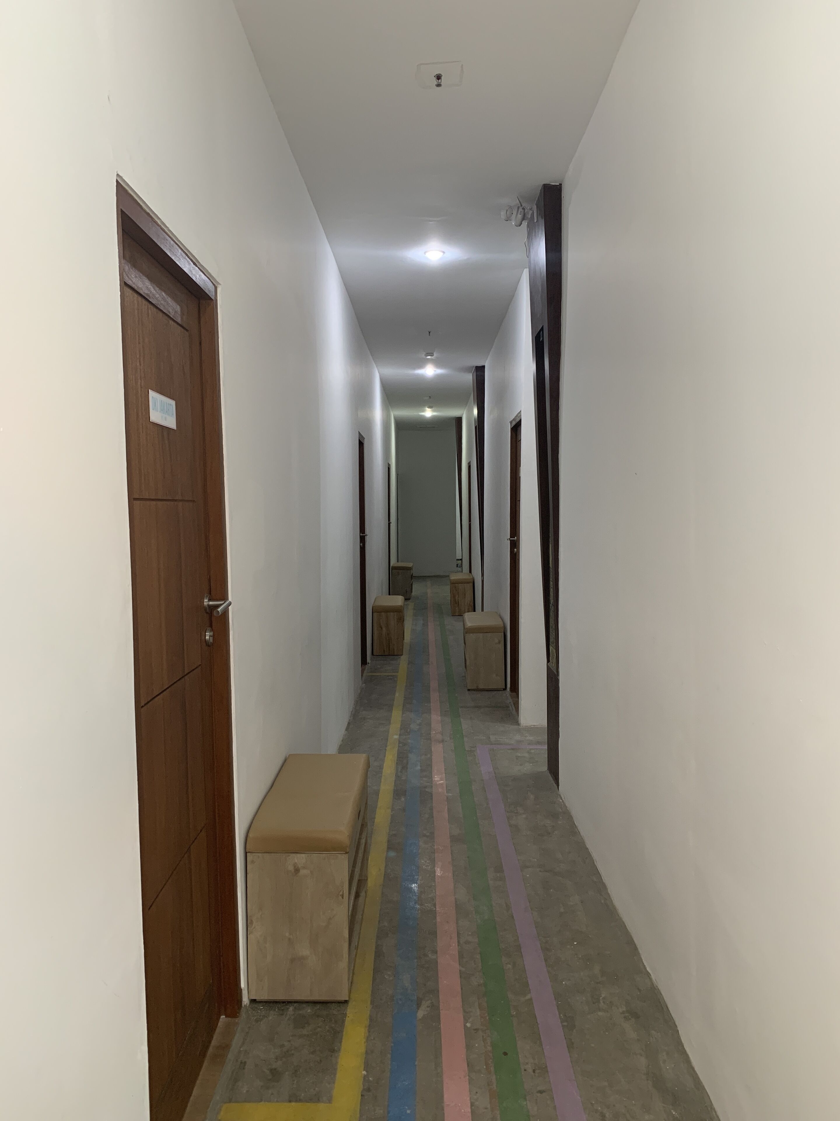 A hallway with wooden doors on either side, a bench in the center, and a rainbow-colored stripe on the floor.