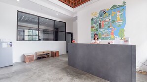 A reception area with a large window, a wooden bench, a grey reception desk, and a wall map. - Fello Bnb Hostel Kuta - Adults Only (Kuta)