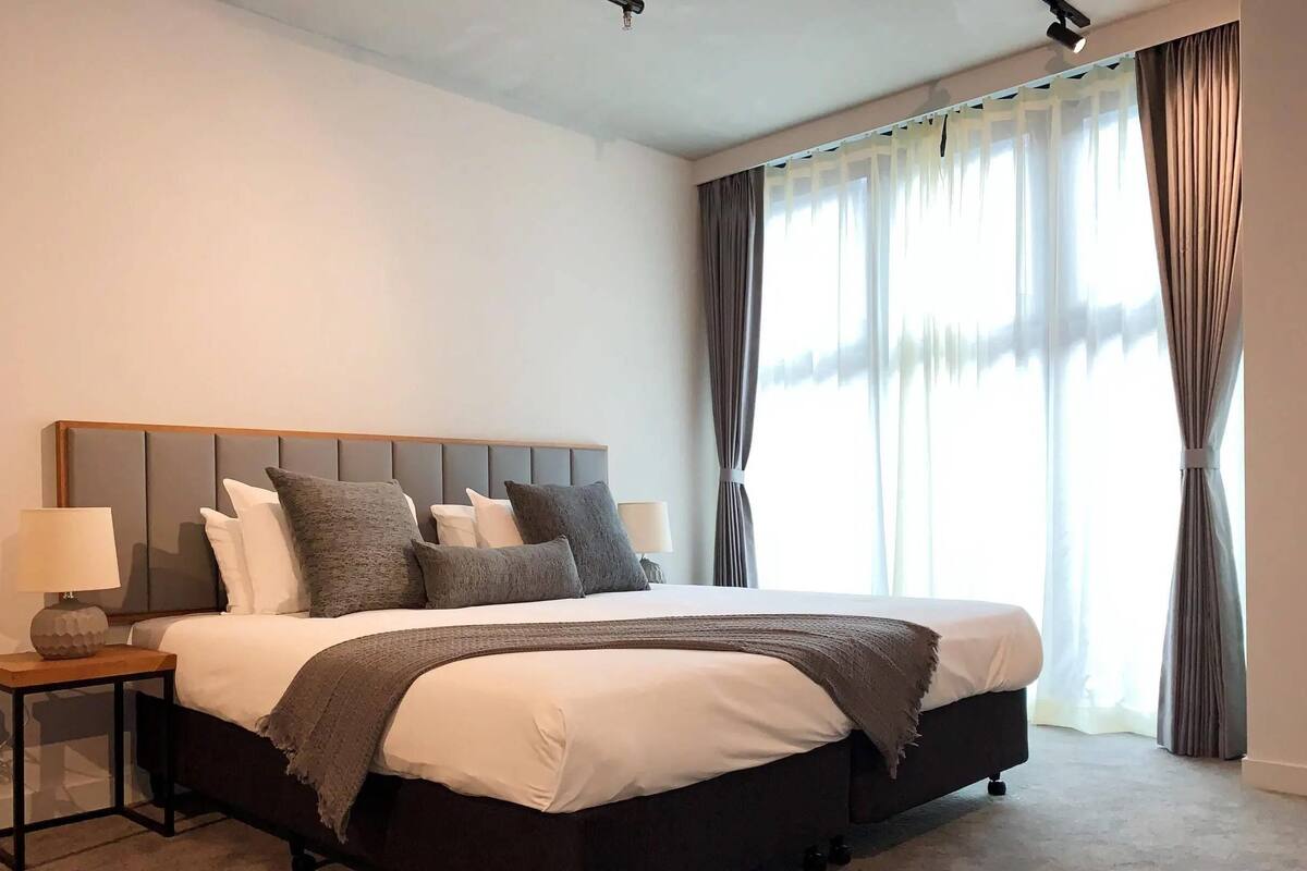 A bedroom with a bed, bedside tables, a lamp, and a window with curtains.