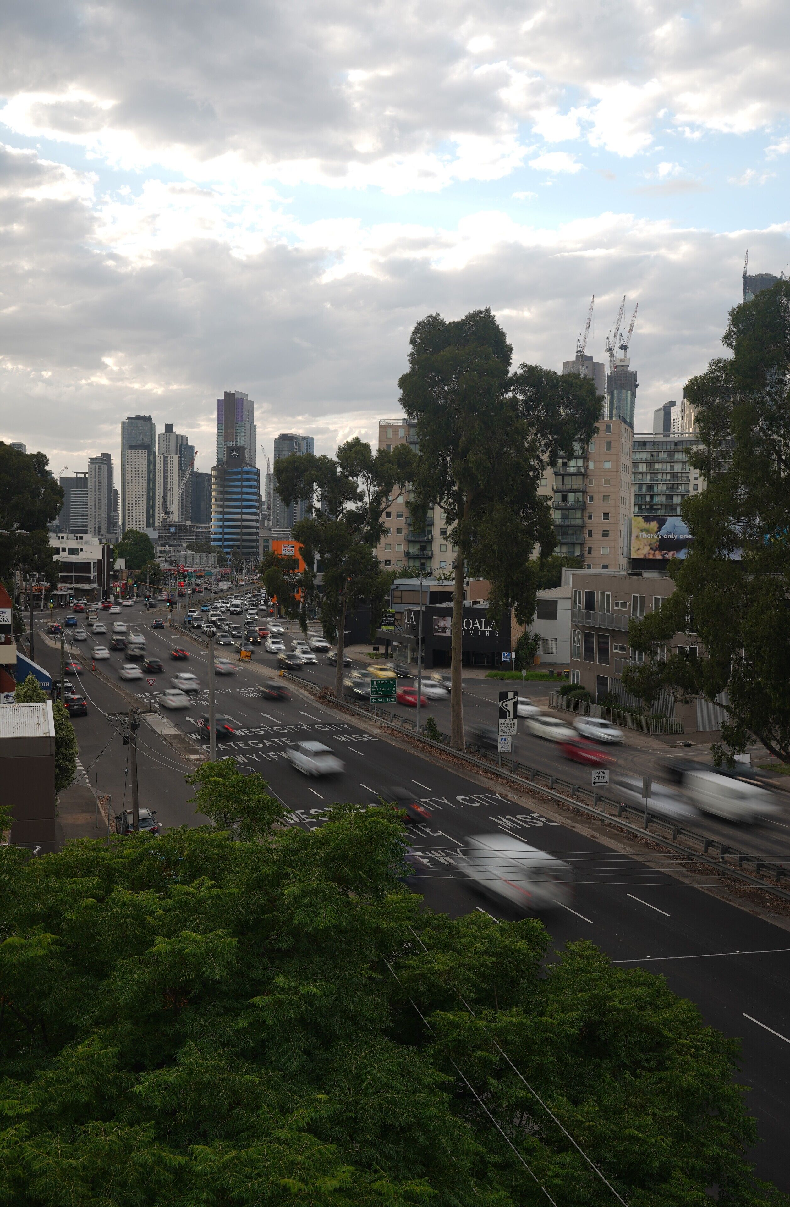 A busy city street with tall buildings, trees, and cars.