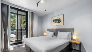 Une chambre d’hôtel avec un grand lit, une table de chevet avec une lampe, une porte-fenêtre coulissante et un tableau encadré au mur.