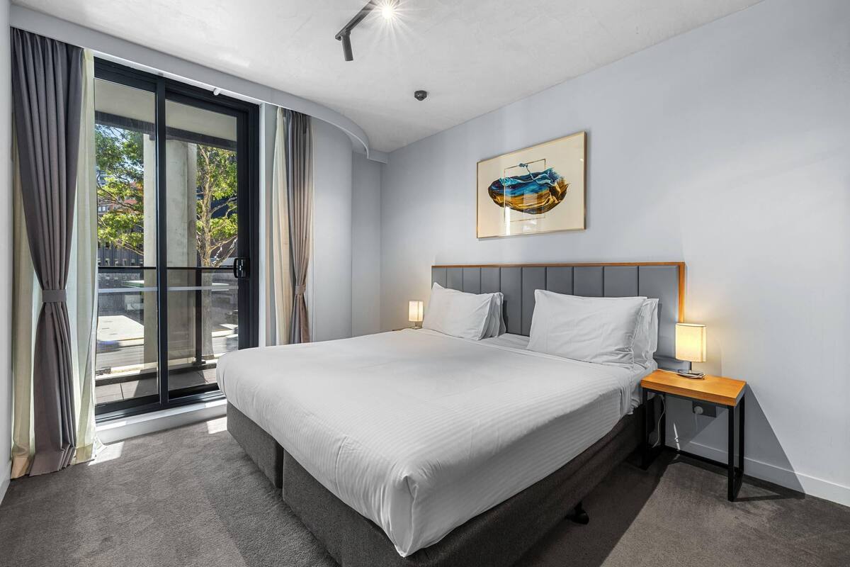 A hotel room with a large bed, a nightstand with a lamp, a sliding glass door, and a framed picture on the wall.