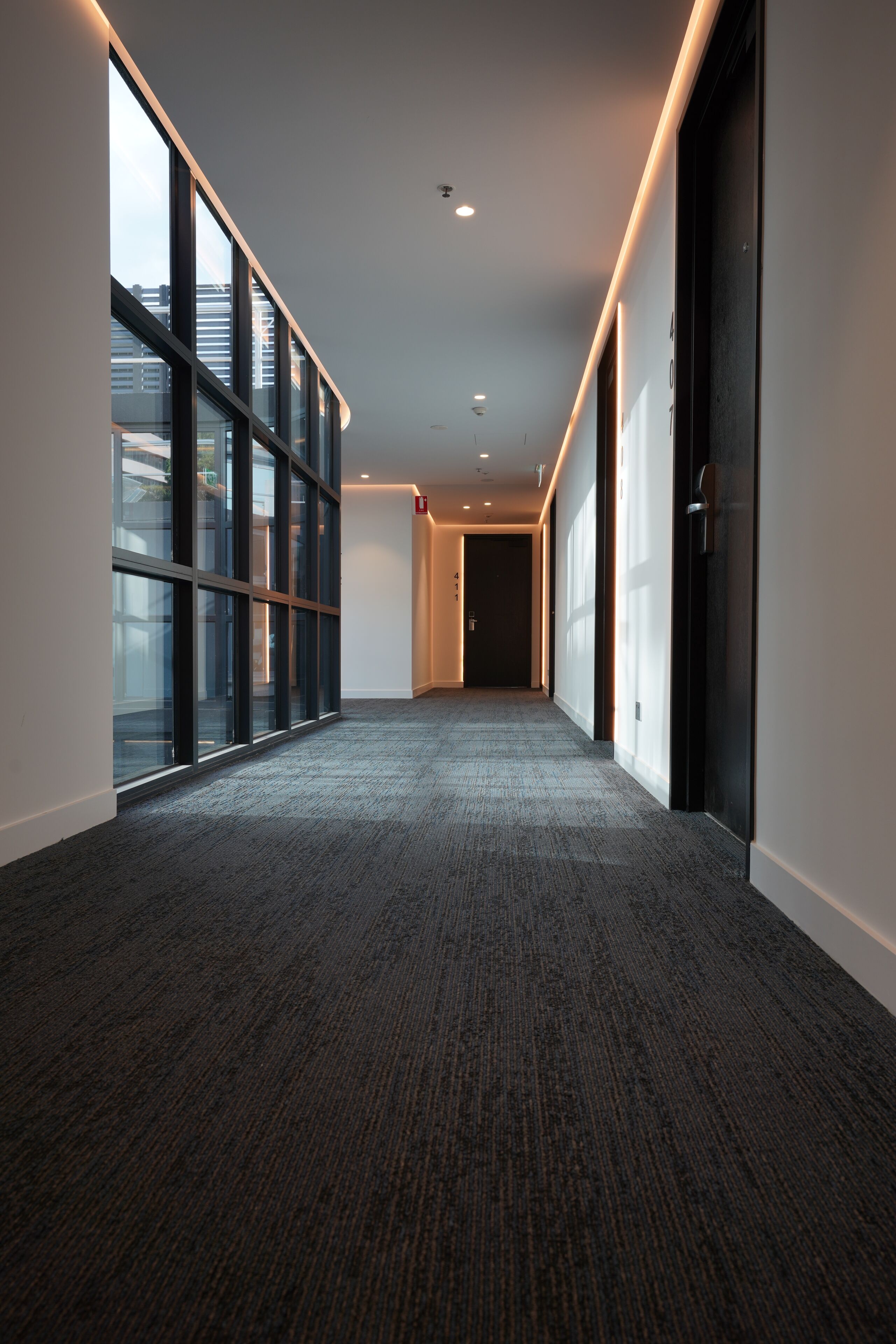 A corridor with glass walls, carpeted floor, and recessed lighting.