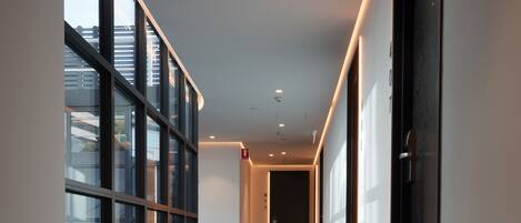 A corridor with glass walls, carpeted floor, and recessed lighting.