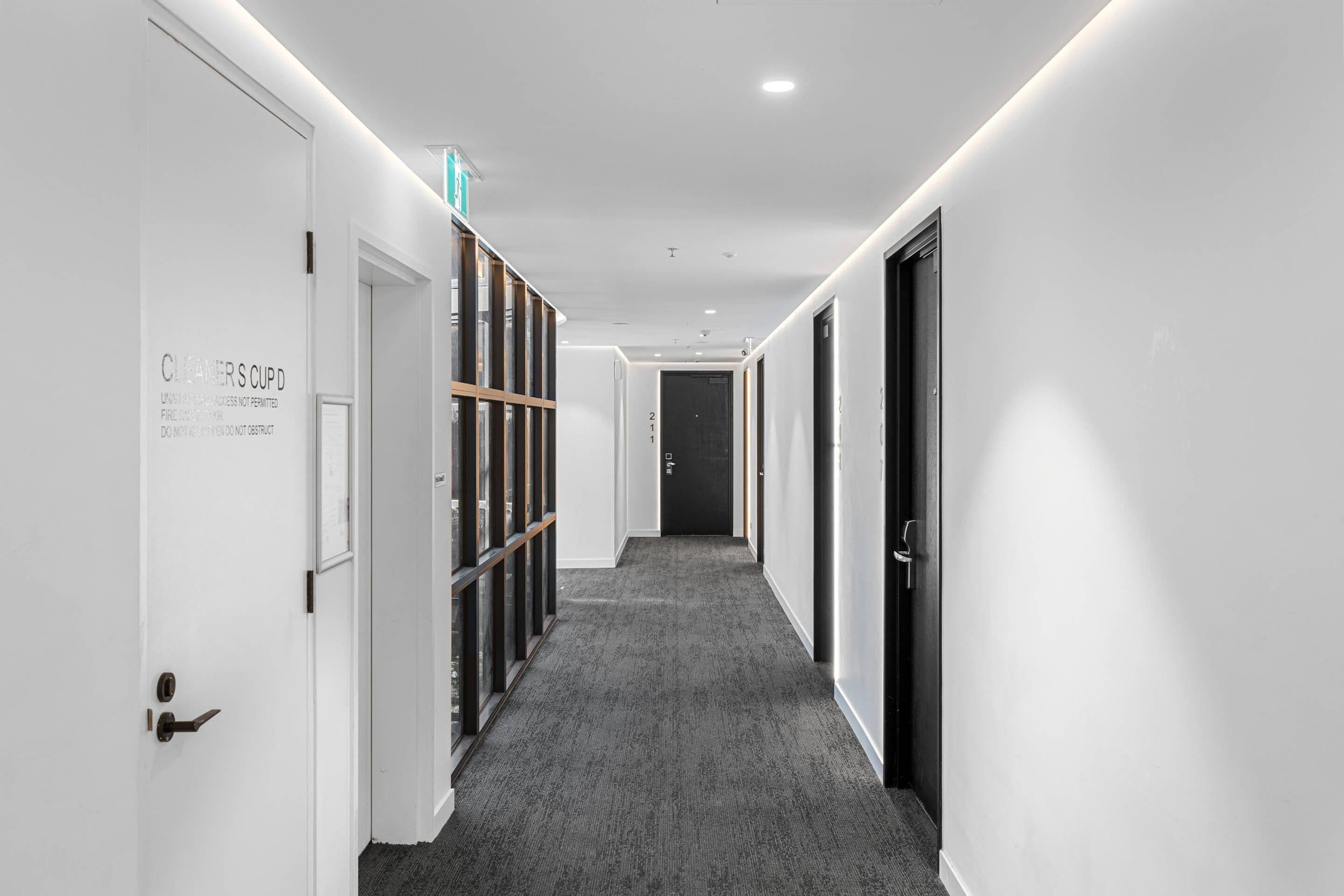 A corridor with white walls, a grey carpet, and doors with a sign.