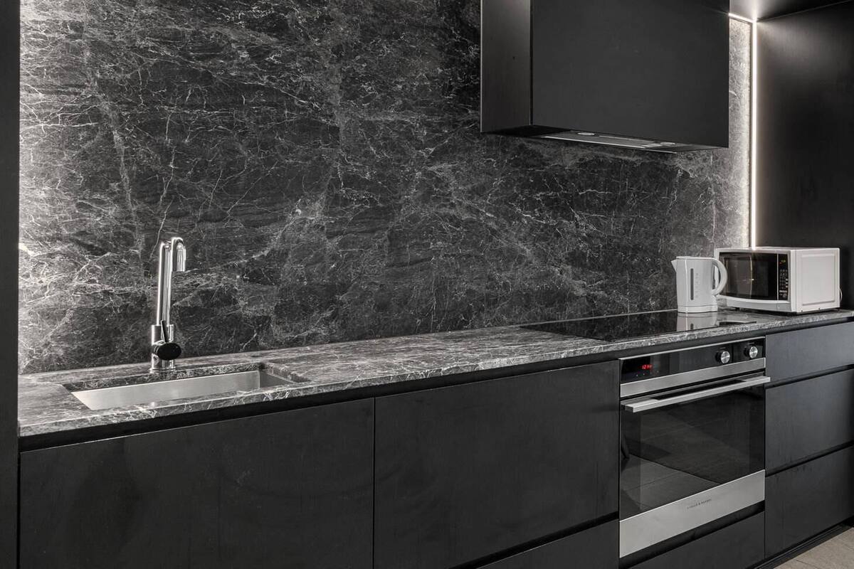 A modern kitchen with a marble backsplash, stainless steel appliances, and a sleek black cabinetry design.