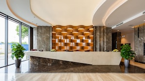A modern reception area with a marble counter, large windows, and potted plants. - Muong Thanh Grand Bai Chay Hotel (Bai Chay)