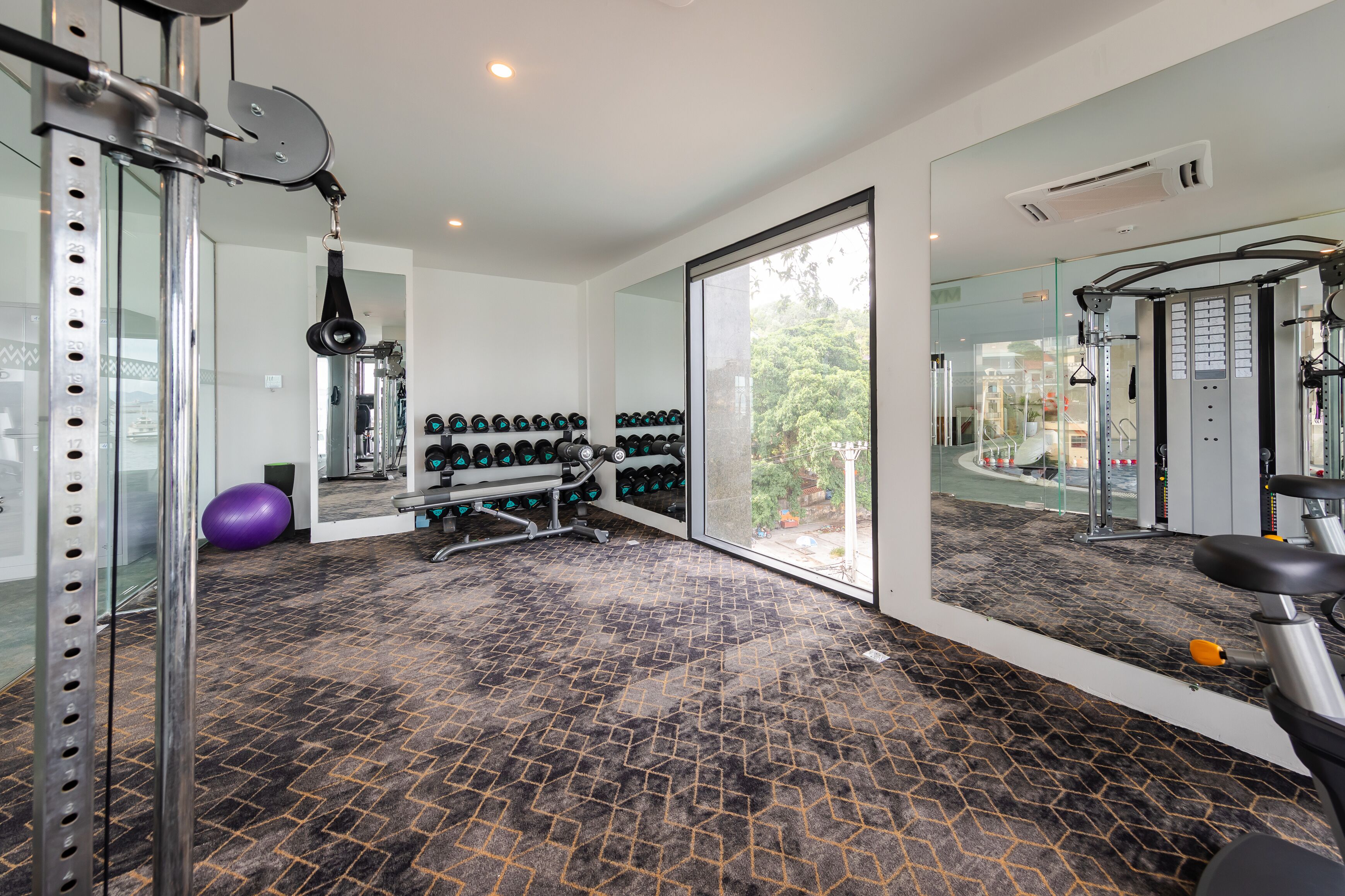 Une salle de sport équipée de matériel d’exercice, dotée d’un murmiroir et d’une grande fenêtre.