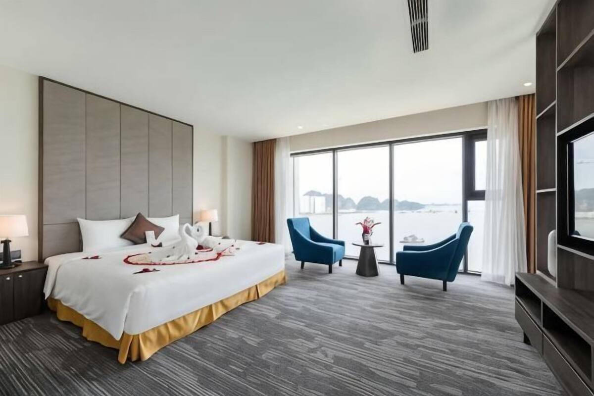 A hotel room with a large bed, two armchairs, a TV, and a view of the water.