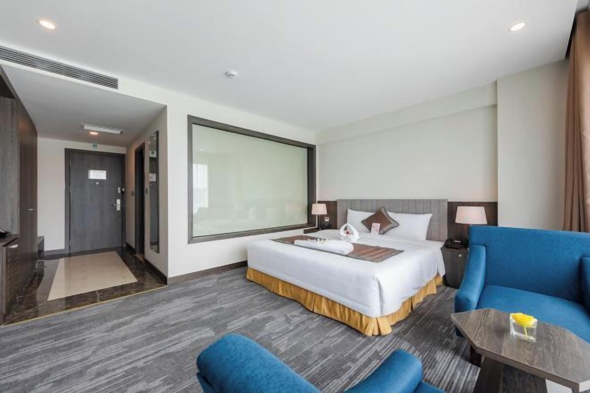 Una habitación de hotel con cama, escritorio, sillón, sofá y un amplio ventanal.