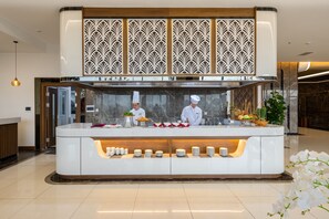 A modern kitchen counter with chefs preparing food, a decorative panel above, and a buffet area with plates and bowls. - Muong Thanh Grand Bai Chay Hotel (Ha Long)