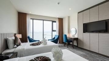A hotel room with two beds, a TV, a desk with a chair, and a view of the sea.