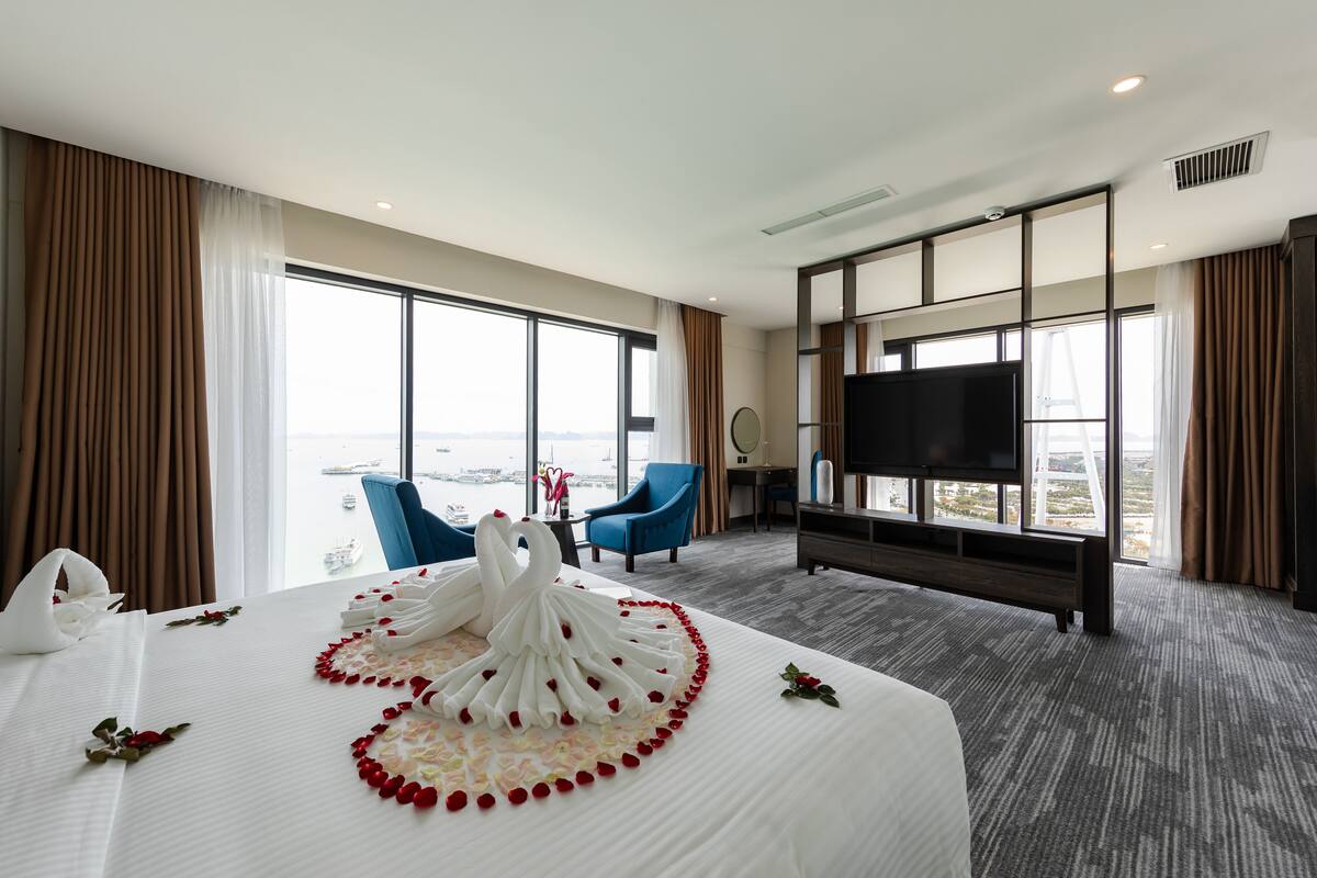 A hotel room with a large bed, a TV, a balcony with a view, and a desk with a chair.