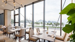 A modern restaurant with large windows, tables set with white napkins, and a view of the cityscape. - Muong Thanh Grand Bai Chay Hotel (Bai Chay)