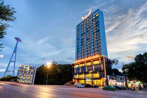 A modern hotel with a prominent sign, multiple floors, and a parking area with cars. - Muong Thanh Grand Bai Chay Hotel (Ha Long)